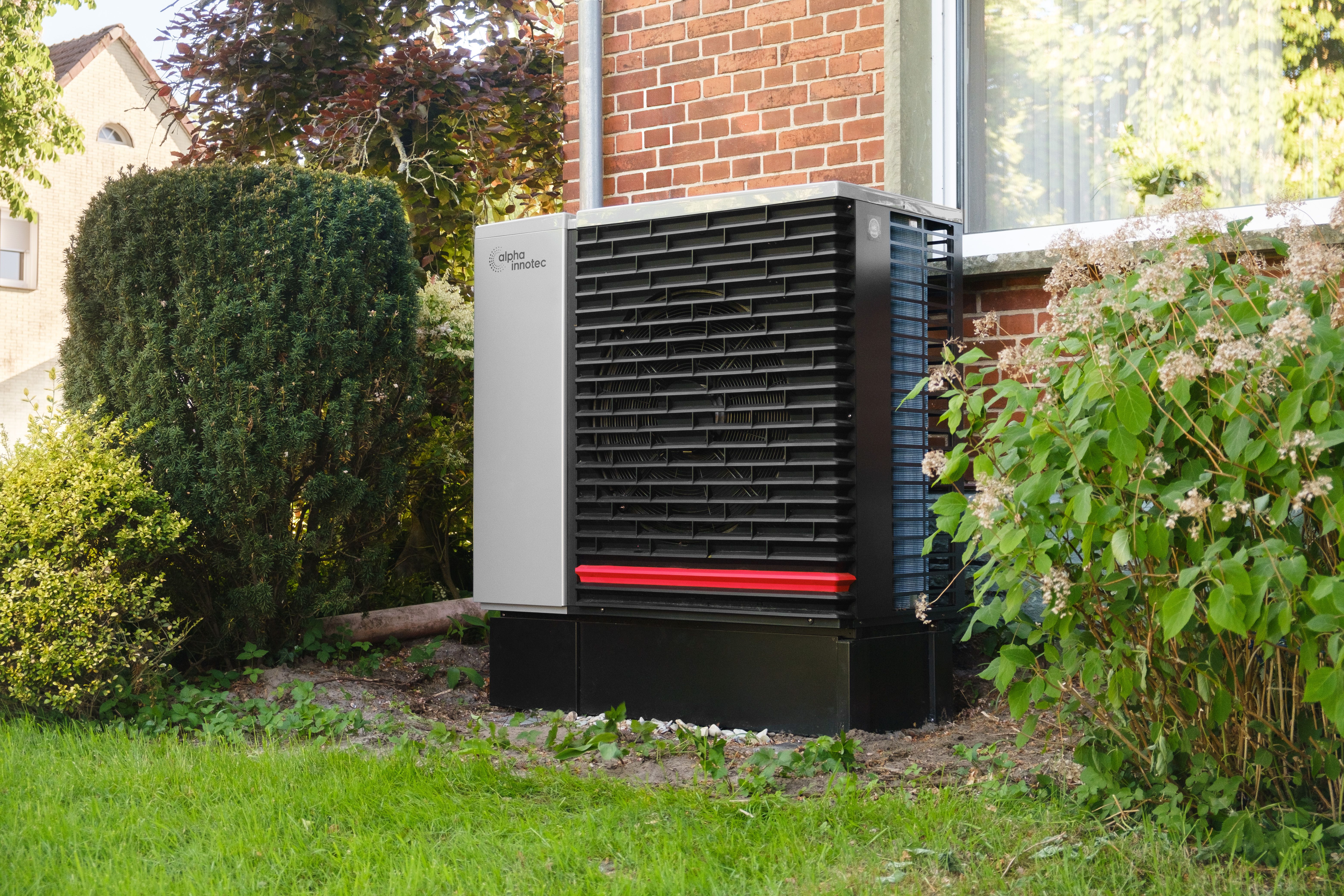 Moderne Wärmepumpe von Alpha Innotec an einer Hauswand zwischen Sträuchern